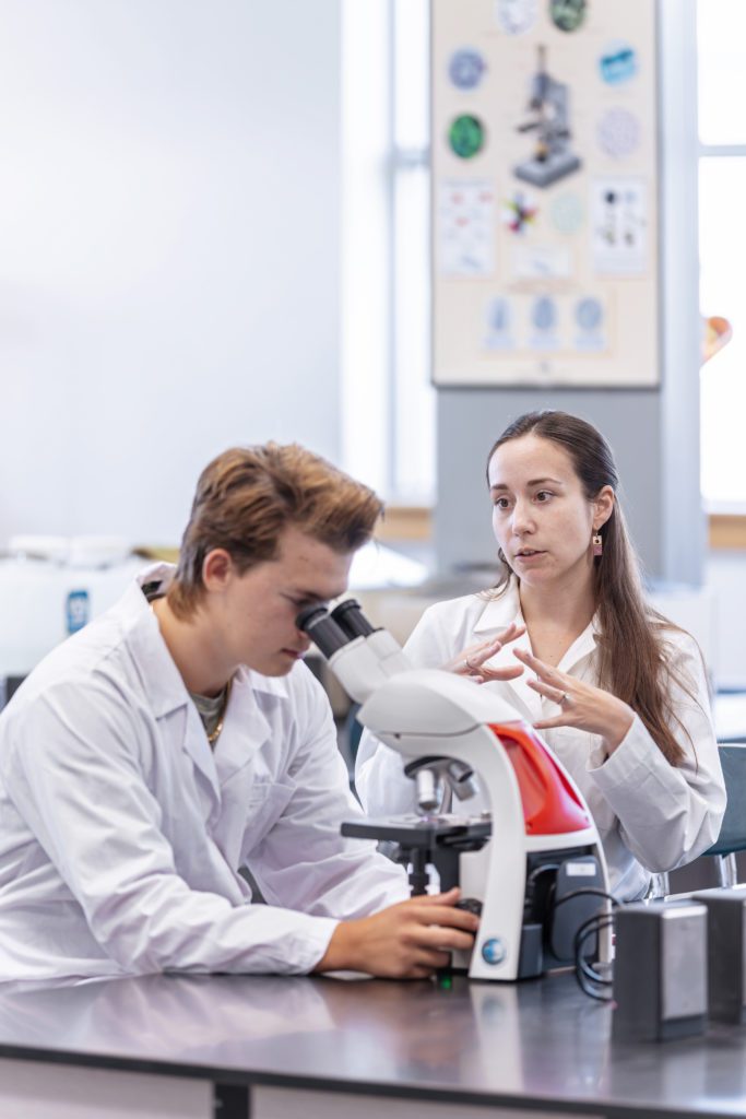 A student using a microscope and Dr. Wentzell in the Biology lab.