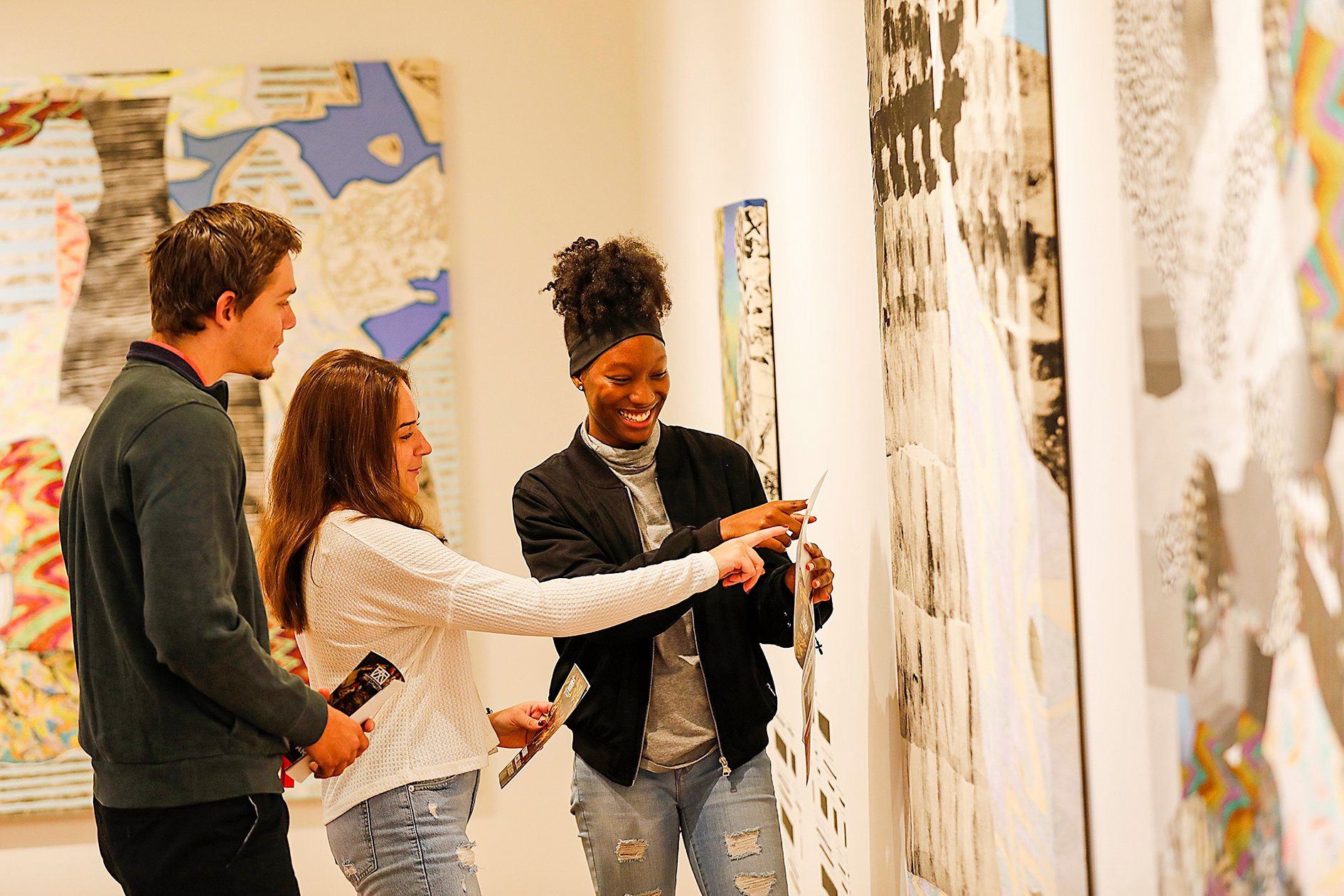 Three students looking at an art on the wall.