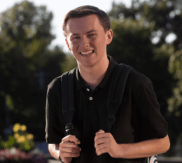 Danie smiling on campus holding backpack outside
