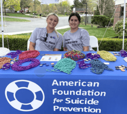 two individuals on campus seated at AFSP table with beads smiling