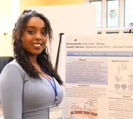 Eliza Doba smiling next to IGNITE research poster at conference