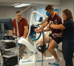 Professor and two sudents using exercise science equipment in lab on campus