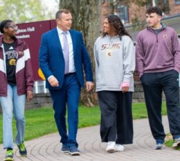 President Daly walking outside of Admissions office with three students