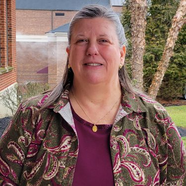 Ann smiling outside wearing eggplant colored shirt with green paisley sweater