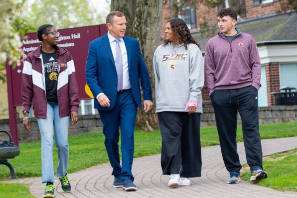 President Daly walking outside of Admissions office with three students